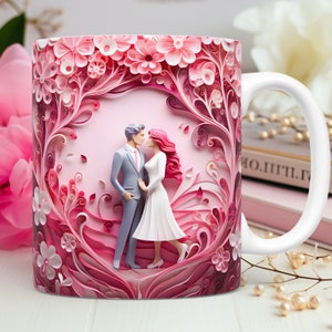 May include: White ceramic mug featuring a romantic design with a couple figurine surrounded by pink paper flowers. The mug has a white handle and a pink background. The design includes a man in a gray suit and a woman in a white dress.