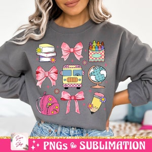 May include: A gray sweatshirt with a colorful design featuring a school bus, books, a globe, a pencil, a backpack, crayons, and bows. The design is perfect for back to school season.
