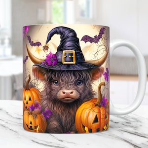 May include: A white ceramic mug with a Halloween-themed design. The design features a brown and white Highland cow wearing a black witch hat with a purple flower and a black buckle. The cow is surrounded by orange pumpkins with jack-o'-lantern faces.