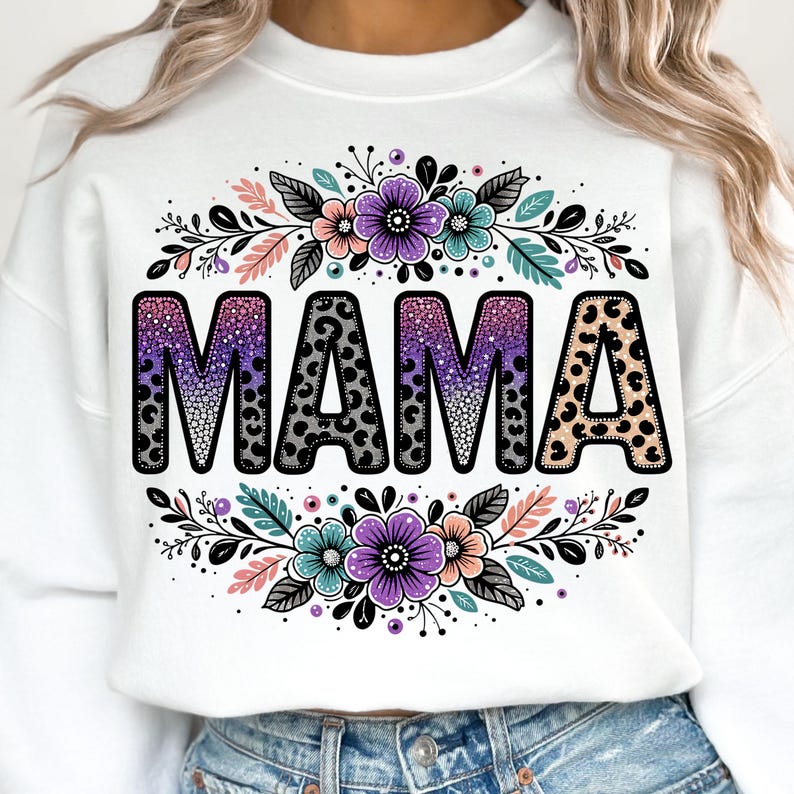 May include: White sweatshirt featuring a purple, pink and black "MAMA" graphic with a leopard print design. The graphic is surrounded by floral designs with pink, purple and teal flowers.