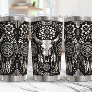 May include: A black and silver stainless steel tumbler featuring a design of a bull skull, dreamcatchers, and feathers. The design is in a southwestern style.