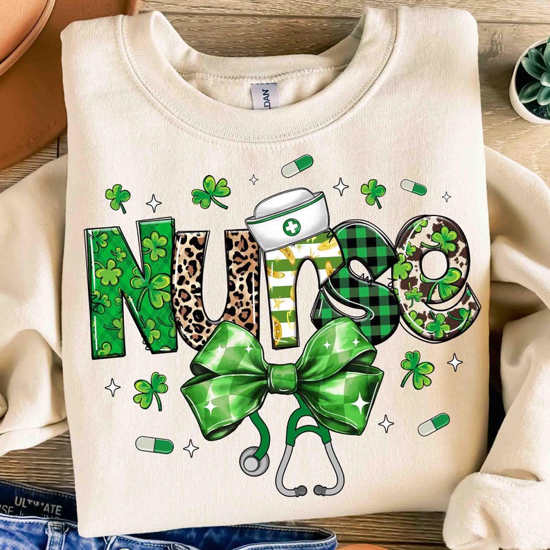 Pu&ograve; includere: Felpa color crema con la scritta "NURSE" in un carattere decorativo. Le lettere presentano trifogli, stampa leopardata e motivi a quadri. Un fiocco verde, uno stetoscopio e un cappello da infermiera completano il design.