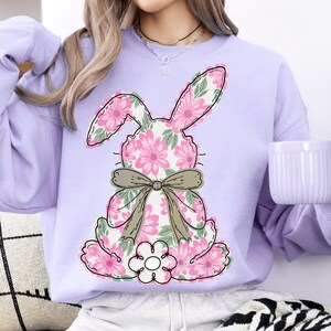 May include: A lavender sweatshirt with a floral bunny design. The bunny is made of pink and green flowers and has a brown bow.