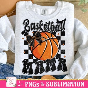 May include: A gray sweatshirt with a black and white checkered background. A basketball with a black bow is in the center of the checkered background. The text "Basketball Mama" is in black with glitter accents.