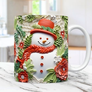 K&ouml;nnte beinhalten: Wei&szlig;e Keramik-Tasse mit einer 3D-Illustration eines Schneemanns mit rotem Hut und Schal, umgeben von gr&uuml;nem Laub und roten Blumen. Der Schneemann hat ein schwarzes Kohlel&auml;cheln und Knopfaugen. Ein festliches Winterdesign.
