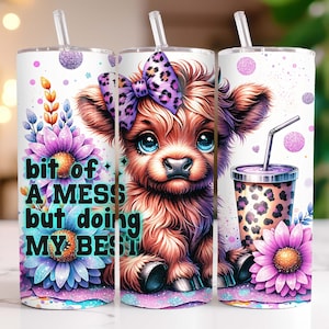 Può includere: Un bicchiere bianco con una mucca Highland marrone e bianca con un fiocco viola. Il bicchiere ha un design floreale viola e blu e il testo "bit of A MESS but doing MY BEST".