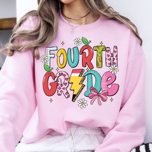 May include: Pink sweatshirt with a colorful graphic that says "FOURTH GRADE" with a rainbow, lightning bolt, hearts, and flowers.