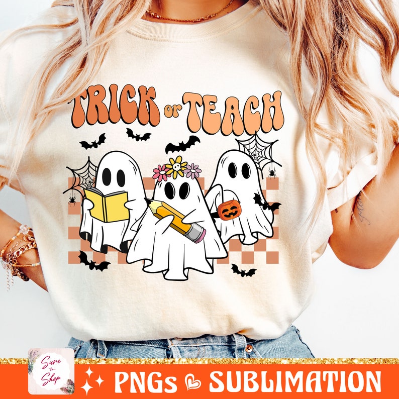May include: A white t-shirt featuring the text "Trick or Teach" in orange and pink lettering. Three cartoon ghosts are positioned below the text, one holding a book, one holding a pencil, and one holding a pumpkin. The ghosts are set against a checkered background with bats and spiderwebs.