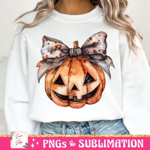 May include: A white sweatshirt with a watercolor illustration of a pumpkin with a brown and white polka dot bow. The pumpkin has a jack-o'-lantern face.