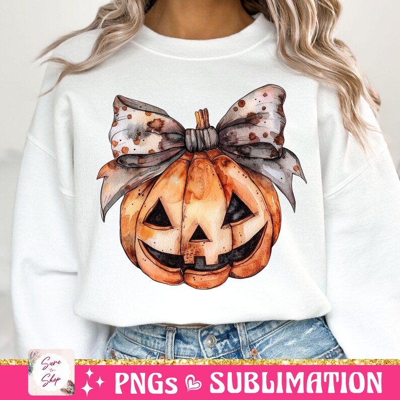 May include: A white sweatshirt with a watercolor illustration of a pumpkin with a brown and white polka dot bow. The pumpkin has a jack-o'-lantern face.
