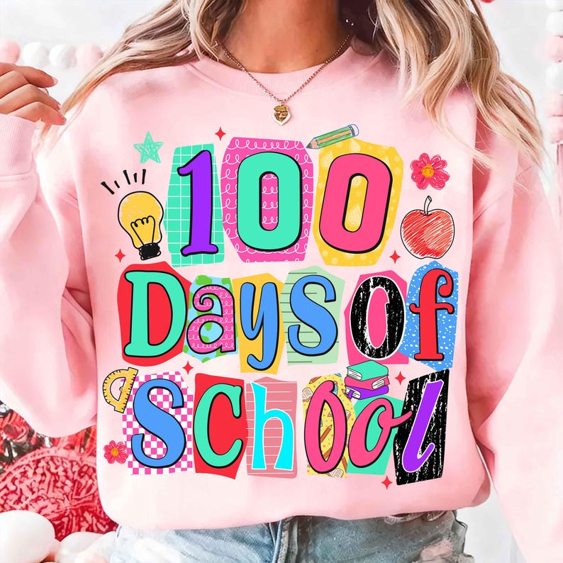 Puede incluir: Sudadera rosa claro con un gr&aacute;fico colorido que dice "100 Days of School". El dise&ntilde;o incluye una bombilla, una manzana, un l&aacute;piz y otros elementos escolares. El texto est&aacute; en varios colores y fuentes.