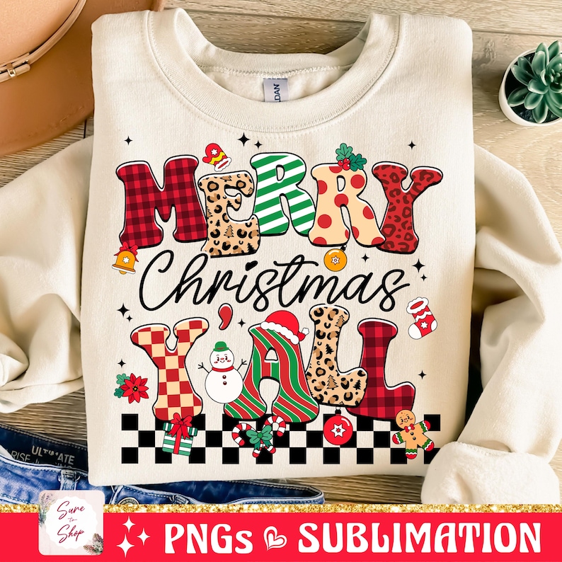 Pu&ograve; includere: Una felpa beige con un design natalizio che presenta il testo "Merry Christmas Y'all" in lettere colorate e decorate. Il design include un pupazzo di neve, un omino di pan di zenzero e un motivo a scacchi.