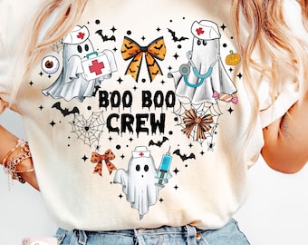 Puede incluir: Una camiseta blanca con un diseño en forma de corazón que presenta lindos fantasmas enfermeras con suministros médicos, un lazo y el texto "BOO BOO CREW".