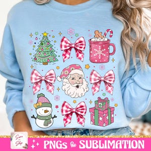 May include: A light blue sweatshirt with a Christmas theme featuring a Santa Claus, a Christmas tree, a snowman, a mug of hot chocolate, and bows with a gingham pattern.