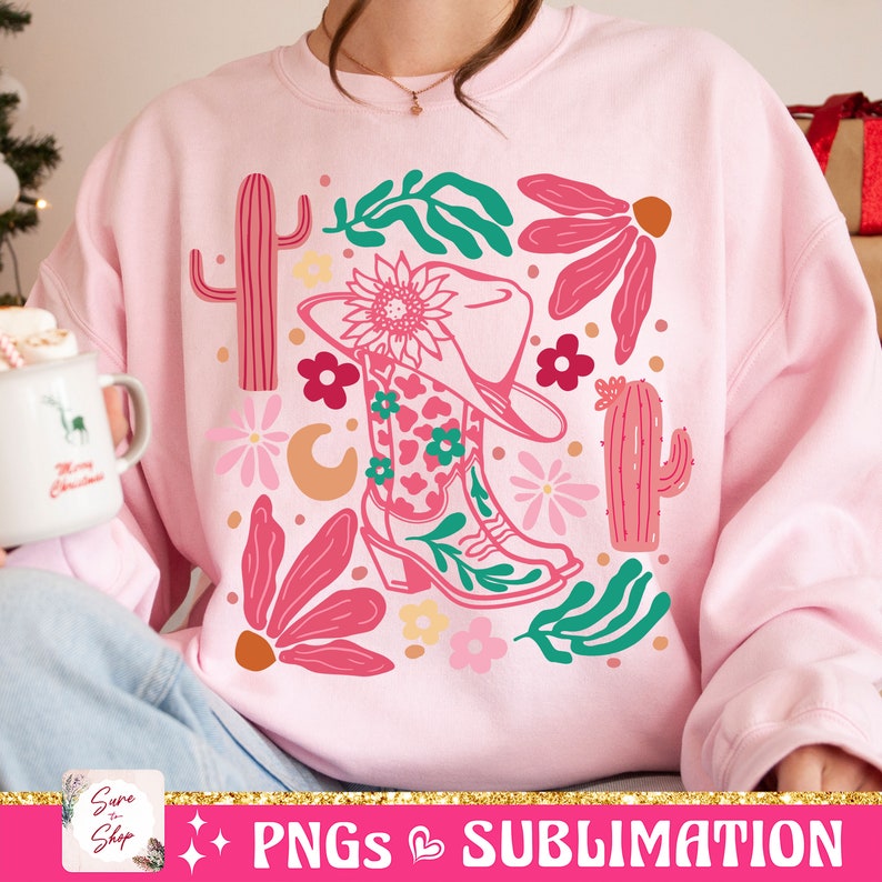 May include: Pink sweatshirt with a colorful graphic of a cowboy boot, hat, flowers, and cacti. The boot has a floral pattern. The design includes a sunflower, crescent moon, and various leaves. The text "PNGs & SUBLIMATION" is at the bottom.