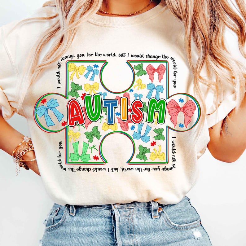 May include: A white t-shirt with a colorful puzzle piece design that says "AUTISM". The puzzle piece is surrounded by colorful bows and the text "I would not change you for the world, but I would change the world for you".