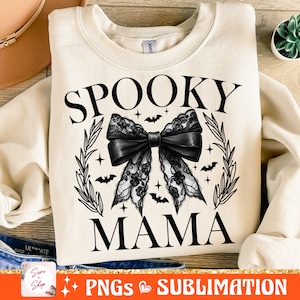 May include: A cream-colored sweatshirt with the text "Spooky Mama" in black. A black lace bow with bats and stars is centered on the sweatshirt.
