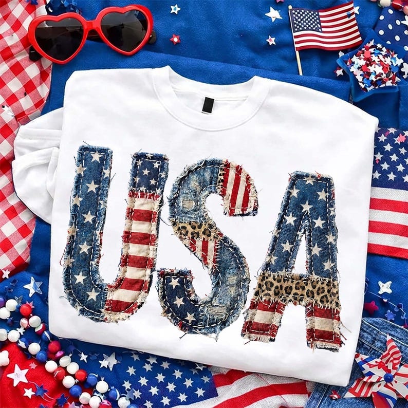 Pu&ograve; includere: Maglietta bianca a maniche lunghe con la scritta "USA" in un design patchwork. Le lettere presentano denim, strisce rosse e bianche, stampa leopardata e tessuto blu con stelle bianche. Tema patriottico con occhiali da sole a forma di cuore.