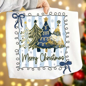 May include: White Christmas-themed pillow with a blue and white striped background. The design features four Christmas trees in shades of gold, green, and blue, with a star on top. The words "Merry Christmas" are written in a script font.