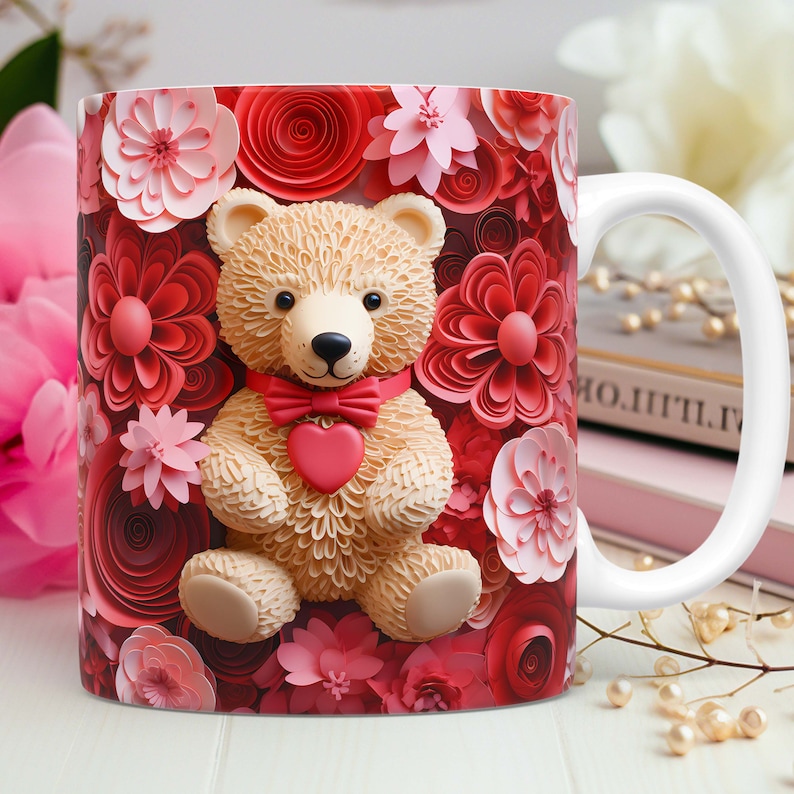 May include: White ceramic mug featuring a teddy bear design with a red bow tie and heart. The mug is decorated with red and pink floral accents. The handle is white.