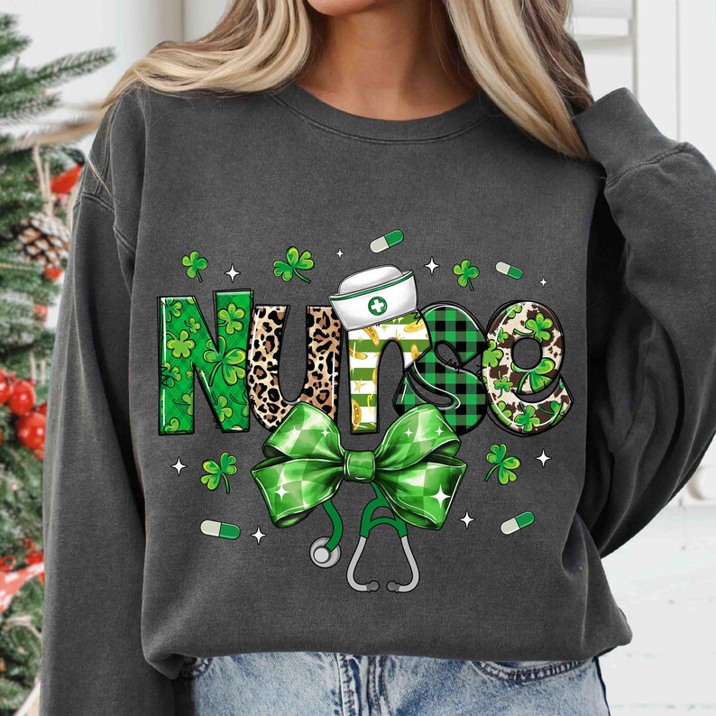 Pu&ograve; includere: Felpa grigio scuro con un design grafico con la parola "Nurse" in verde, stampa leopardata e motivi a quadri. Un fiocco verde, uno stetoscopio, trifogli e pillole completano il design.