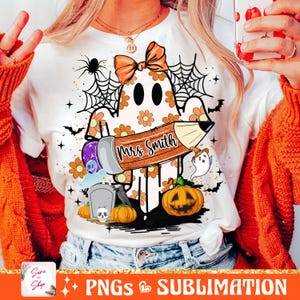 Puede incluir: Una camiseta blanca con un fantasma sosteniendo un l&aacute;piz que dice "Mrs. Smith". El fantasma lleva un lazo y hay otras decoraciones de Halloween a su alrededor, incluyendo una telara&ntilde;a, murci&eacute;lagos, una calabaza y una l&aacute;pida.
