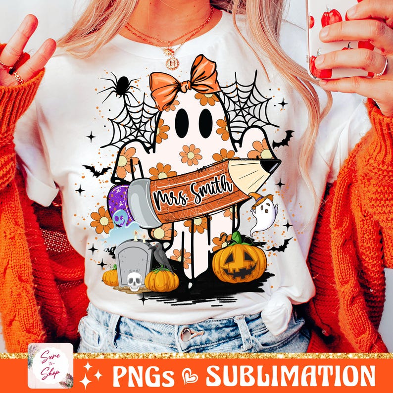 Puede incluir: Una camiseta blanca con un fantasma sosteniendo un l&aacute;piz que dice "Mrs. Smith". El fantasma lleva un lazo y hay otras decoraciones de Halloween a su alrededor, incluyendo una telara&ntilde;a, murci&eacute;lagos, una calabaza y una l&aacute;pida.