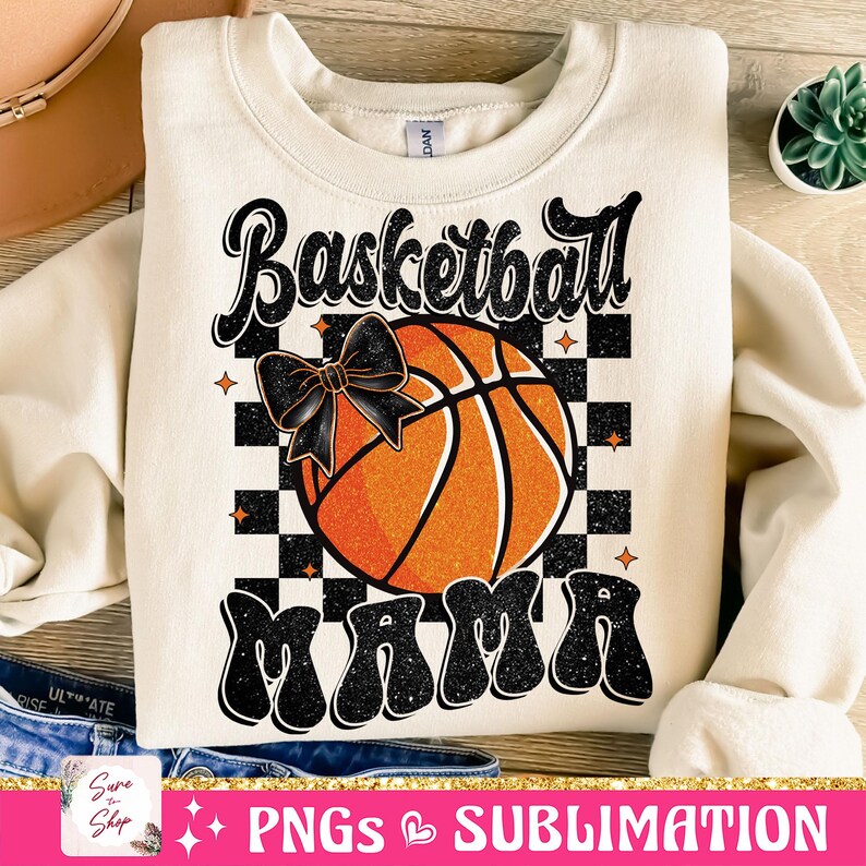 May include: A beige sweatshirt with a black and orange basketball graphic and the text "Basketball Mama" in black with a glittery effect.
