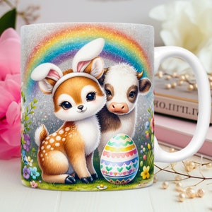 May include: White ceramic mug featuring a colourful illustration of a deer wearing bunny ears, a cow, and an Easter egg. The background includes a rainbow and flowers.