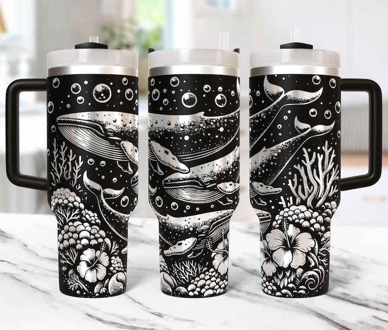 May include: Black and silver insulated tumbler featuring a whale and ocean life design. The tumbler has a black handle and lid, with a white straw. The design includes whales, coral, and bubbles.