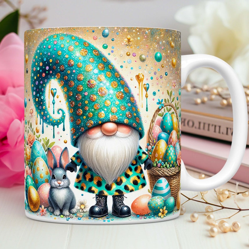 May include: A white ceramic mug featuring a colourful illustration of a gnome holding a basket of Easter eggs. The gnome is wearing a teal and gold hat and a teal and leopard print coat. A grey bunny is standing next to the gnome.