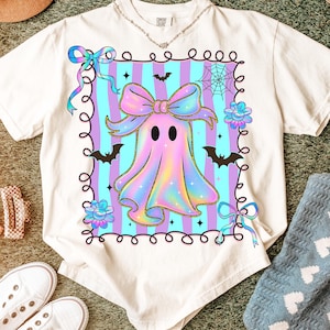 Puede incluir: Camiseta color crema con un dise&ntilde;o de fantasma pastel, un gran lazo, murci&eacute;lagos y flores. El fantasma est&aacute; rodeado por un marco decorativo con un fondo a rayas. Un dise&ntilde;o divertido y caprichoso para Halloween.