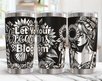 May include: A stainless steel tumbler with a black background and a silver design. The design features a woman with a sunflower in her hair, a sunflower in her hand, and the text "Let Your Dreams Bloom".