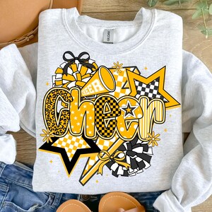 May include: A light gray sweatshirt with a vibrant "CHEER" graphic in yellow, black, and white. The design includes stars, pom-poms, and a megaphone, with a leopard print "C". The word "CHEER" is the focal point.