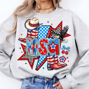 May include: Gray sweatshirt with a graphic print of a cowboy hat, boots, and an eagle with the word "USA" in red, white, and blue.