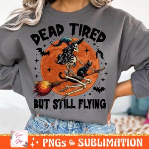 May include: A gray sweatshirt with the text "Dead Tired But Still Flying" in black. A skeleton witch with black hair and a black cat flies on a broomstick in front of a red moon with orange stars.