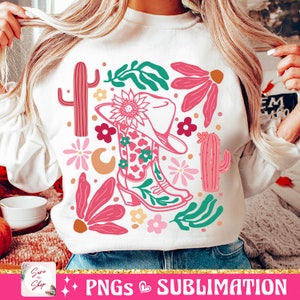 May include: White sweatshirt featuring a colorful western-themed design. The graphic includes a cowboy hat, boots, cacti, flowers, and the text "PNGs & Sublimation". The design incorporates pink, green, and orange elements.