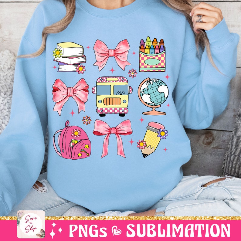 May include: A light blue sweatshirt with a design of school-themed illustrations. The design includes a school bus, a globe, a backpack, a pencil, crayons, books, and pink bows.