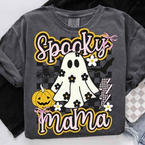 Puede incluir: Sudadera gris oscuro con un dise&ntilde;o de Halloween. El dise&ntilde;o presenta un fantasma con flores, una calabaza, una ara&ntilde;a, un murci&eacute;lago y las palabras "Spooky Mama" en una fuente retro. Los lazos rosas y los rayos completan el dise&ntilde;o.