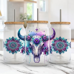 Puede incluir: Tres vasos blancos con tapa de madera y una pajita de acero inoxidable. Cada vaso presenta un diseño diferente. Uno tiene un mandala morado y azul, otro tiene una calavera morada y azul con flores, y el último tiene un mandala morado y azul.