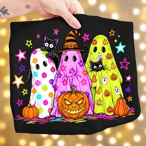 May include: A black t-shirt featuring a graphic of three ghosts. One ghost has colorful polka dots, one wears a witch hat with flowers, and one is lime green with small pumpkins. Two black cats and a large jack-o'-lantern are included.
