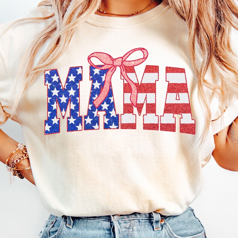 May include: A white t-shirt with a red, white, and blue "MAMA" graphic with a pink bow on top. The graphic is designed to look like the American flag.