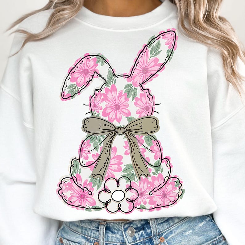 May include: White sweatshirt with a pink floral bunny design. The bunny has a brown bow and is sitting down.