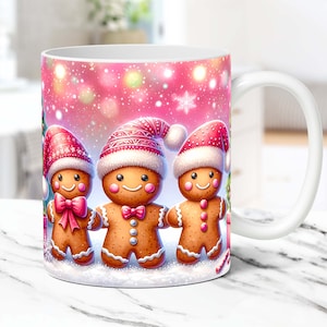 May include: White ceramic mug with a pink background and three gingerbread people wearing Santa hats. The gingerbread people are smiling and holding hands. The background is decorated with white snowflakes and pink lights.