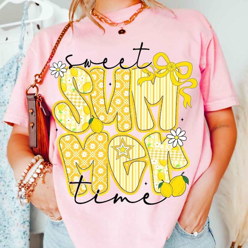 以下が含まれることがあります： ピンク色のTシャツ。黄色いレモンをテーマにしたデザインで「Sweet Summer Mom Time」の文字が描かれています。レモン、デイジー、リボンがデザインされています。カジュアルな夏のテーマの衣料品です。