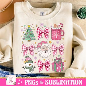 May include: A cream-colored sweatshirt with a Christmas-themed design. The design features a green Christmas tree, a snowman, Santa Claus, pink and white gingham bows, a pink mug with marshmallows and a candy cane, and a pink gift box with green wrapping paper.