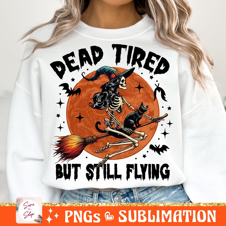 May include: A white sweatshirt with a graphic design of a skeleton witch riding a broomstick with a black cat. The text "Dead Tired But Still Flying" is printed on the sweatshirt.
