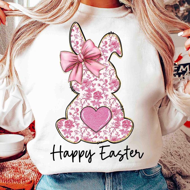 Op de afbeelding: Witte trui met een roze konijn ontwerp en de tekst "Happy Easter". Het konijn heeft een roze strik en een roze hart op zijn borst.