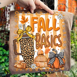 May include: A brown graphic featuring the text "FALL BASICS" in orange and gold. The design includes a leopard print tumbler, a knitted hat, a pumpkin with a plaid bow, and autumn leaves.