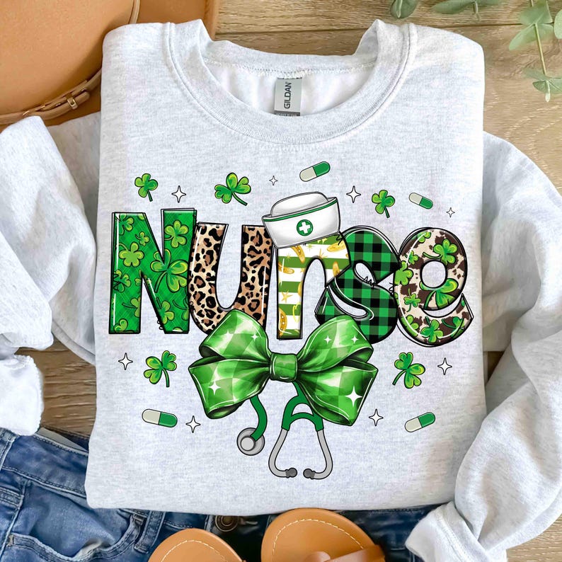 Pu&ograve; includere: Una felpa grigio chiaro con la scritta "NURSE" in un design decorativo. La "N" &egrave; verde con trifogli, la "U" &egrave; con stampa leopardata, la "R" &egrave; gialla e bianca, la "S" &egrave; a quadri neri e verdi e la "E" &egrave; verde con trifogli. Sono presenti anche un fiocco verde e uno stetoscopio.